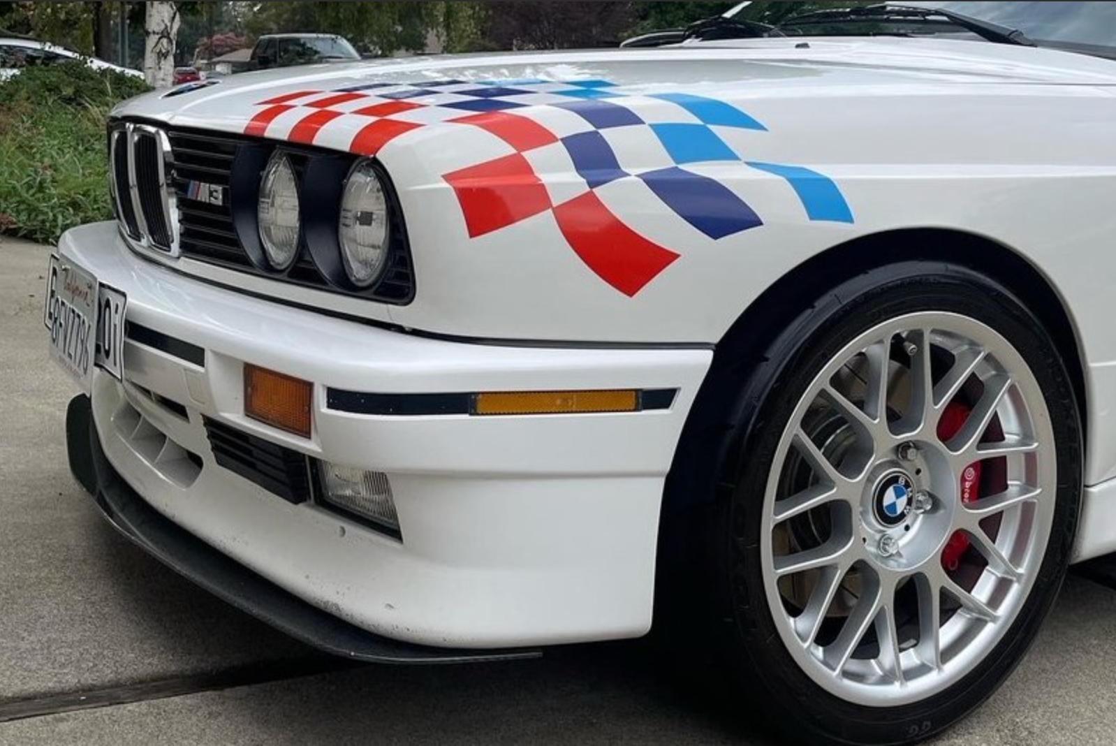 White BMW M3 with checkered flag graphics on the hood and silver wheels.