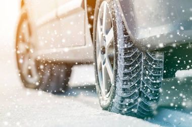Car tires with snow treads driving on a snow-covered road during a snowfall.