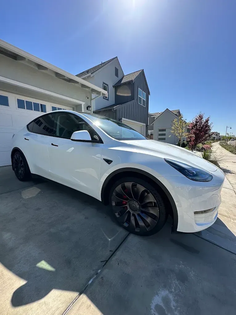 White Tesla Model Y parked in front of a modern house on a sunny day.