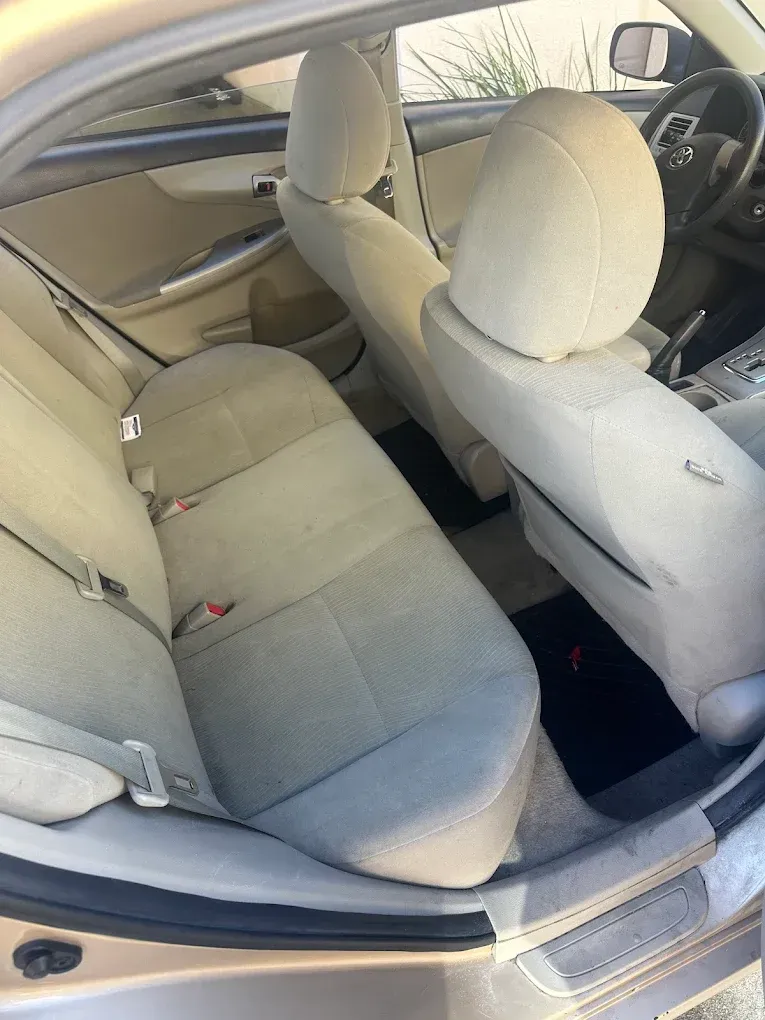 Interior of a tan Toyota Corolla with gray cloth seats. Rear seats are visible. Black floor mat.