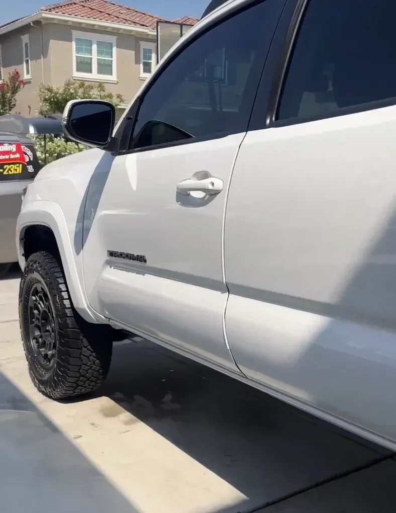 White Toyota Tacoma truck with black wheels and tinted windows parked outside.