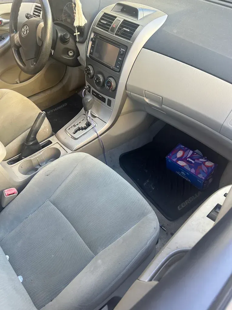 Interior of a Toyota Corolla. Gray seats, dashboard, and console. A tissue box sits in the passenger footwell.