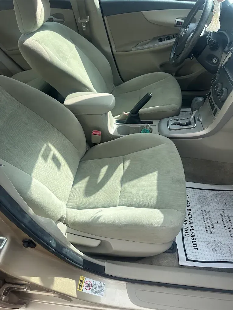 Tan interior of a car, focusing on front seats. Includes steering wheel, center console, and newspaper on the floor.