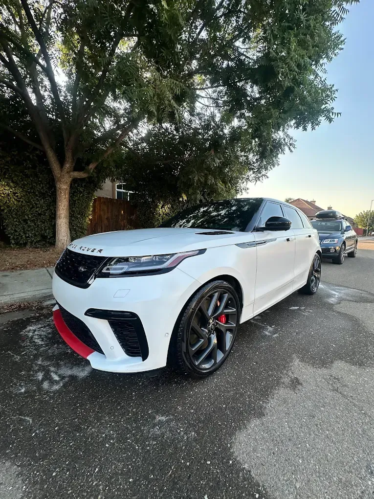 White Range Rover Velar parked on a street with a red front splitter, black wheels, and tinted windows.