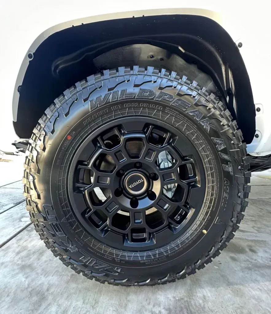 Black off-road tire and rim on a white vehicle. The tire has a deep tread.