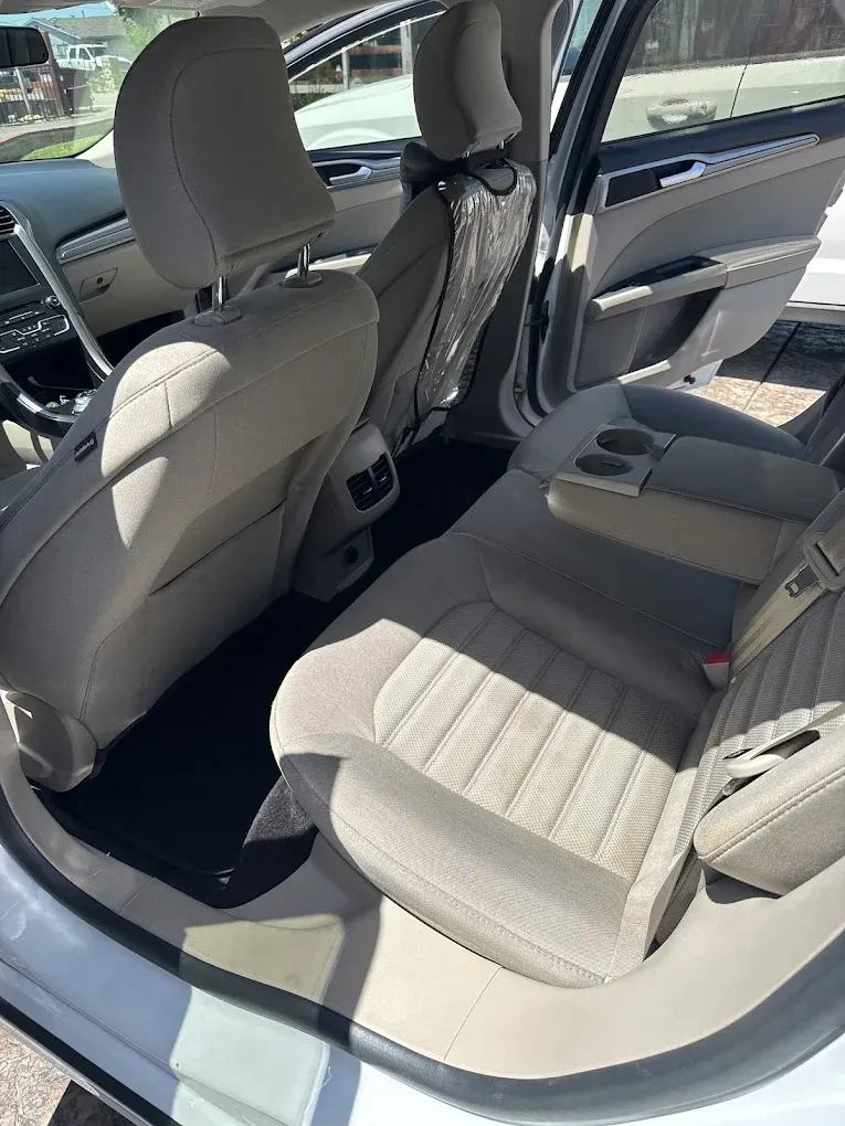 Interior of a light-colored car. Beige fabric seats, black floor mats. Open back doors.