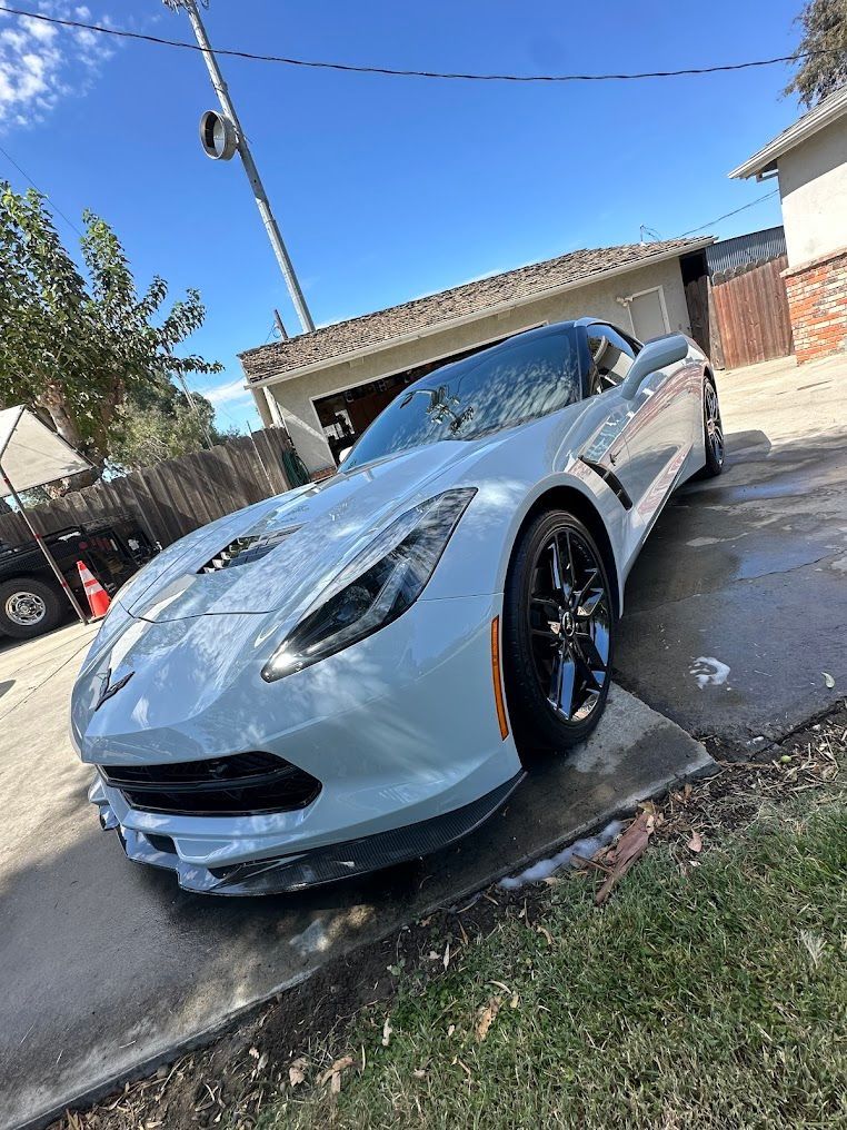 Gray Chevrolet Corvette parked on a wet driveway, sunny day.