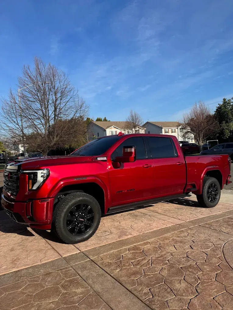 Red GMC Sierra truck with black wheels parked on a patterned driveway under a blue sky.