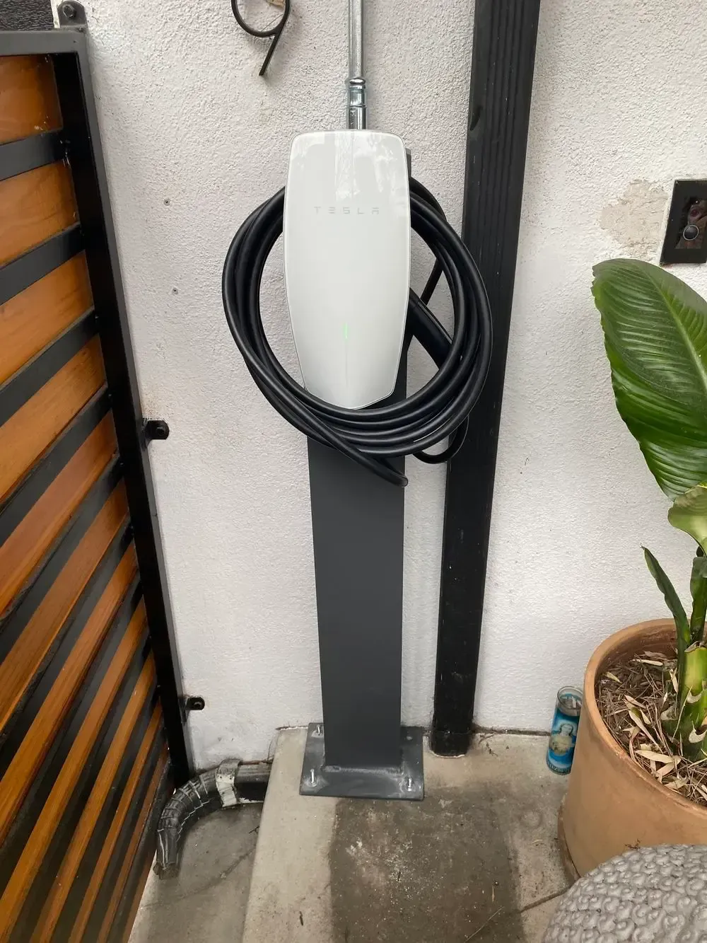 Tesla electric vehicle charger mounted on a black pole, with coiled black cable.