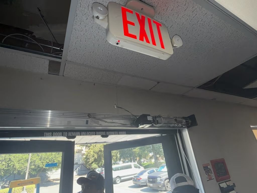 Bright red EXIT sign above a doorway. Wires and ceiling tiles are damaged.