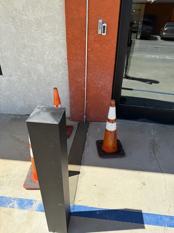Orange traffic cones and a black post near a building entrance with a ramp.