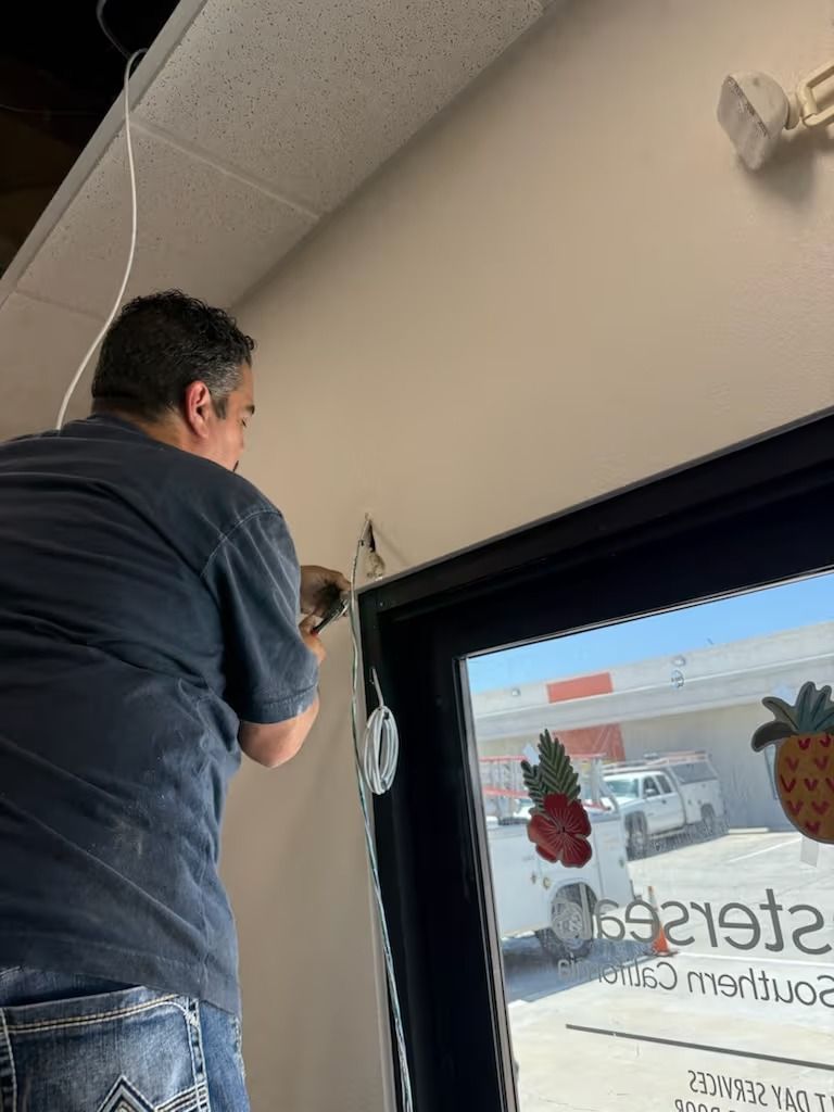 Person on ladder, installing electrical fixture near a window. White wall, black trim.