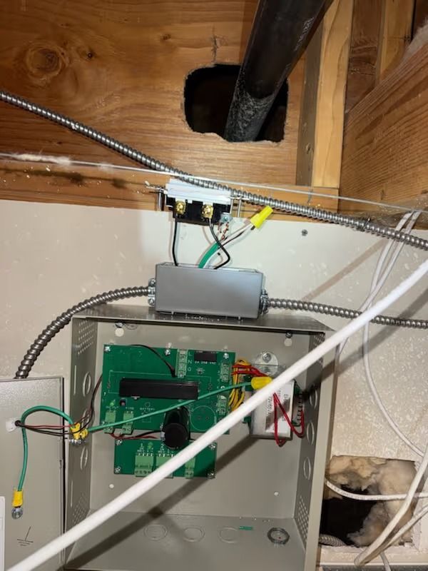 Electrical panel with wires and circuit board in a wooden-framed wall. Cables and conduits are visible.