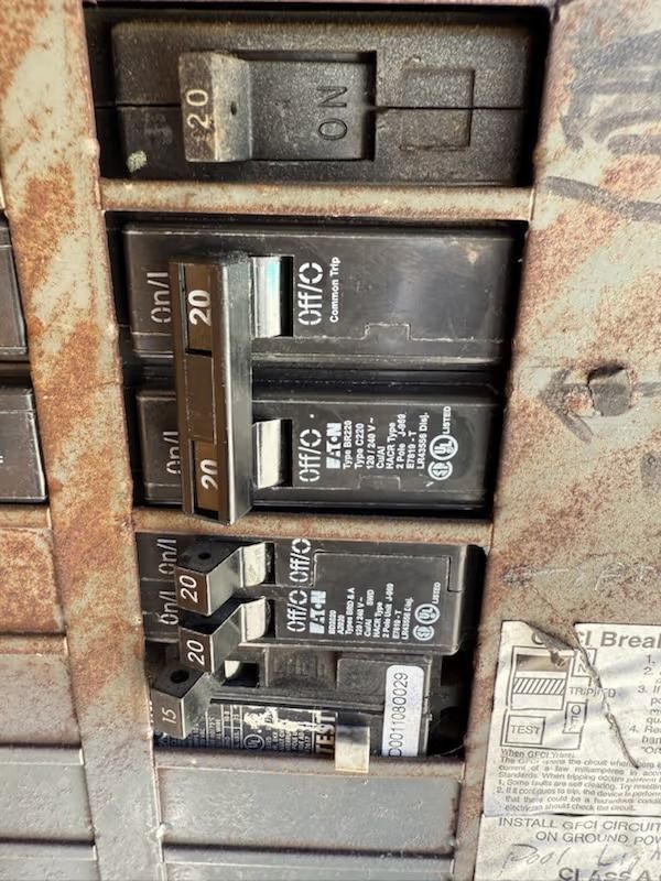 Close-up of a rusty electrical breaker box with various breakers in the on and off positions; 20 amp labels.
