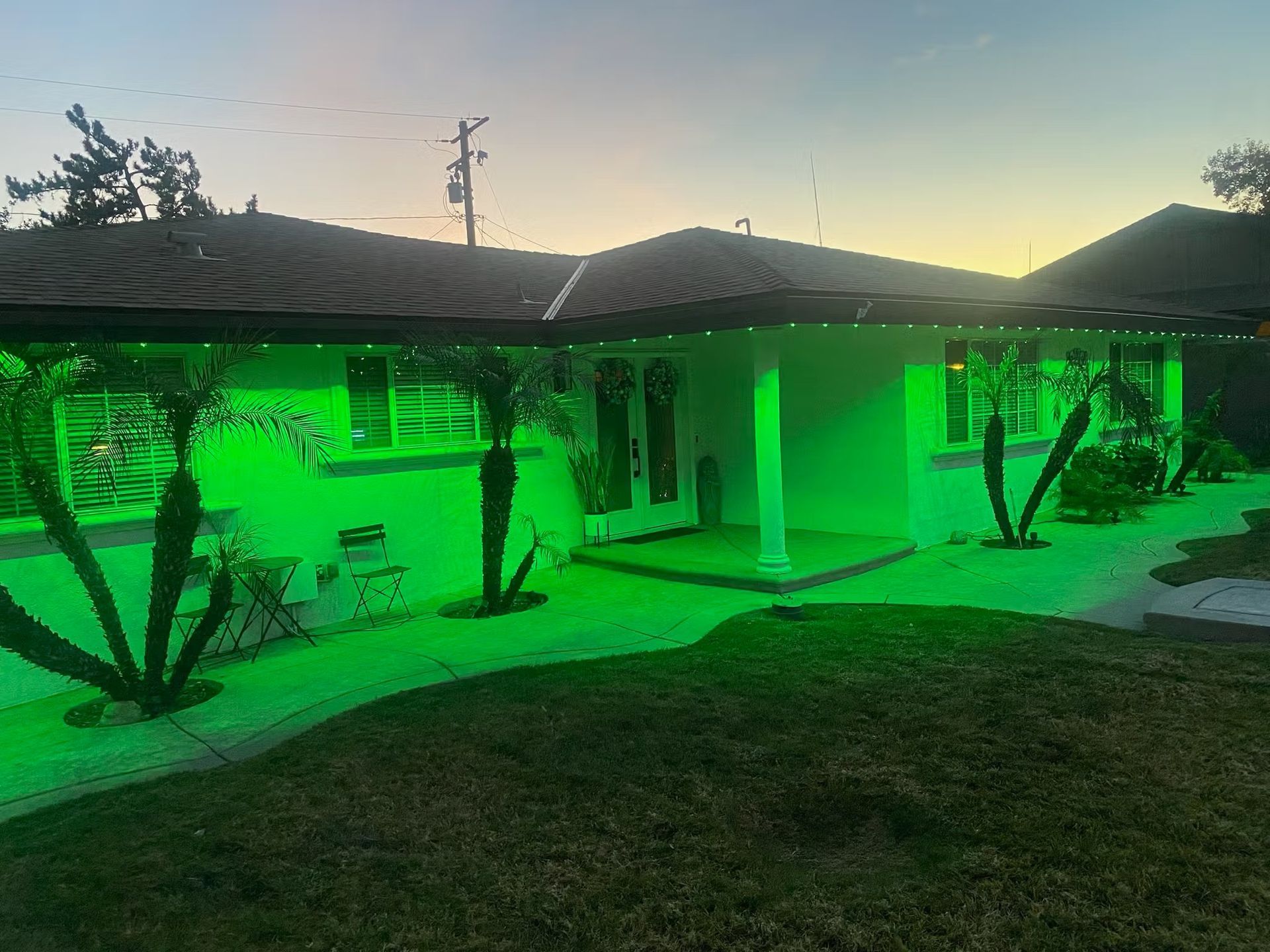 House exterior illuminated with green lights along the roof and landscape at dusk.