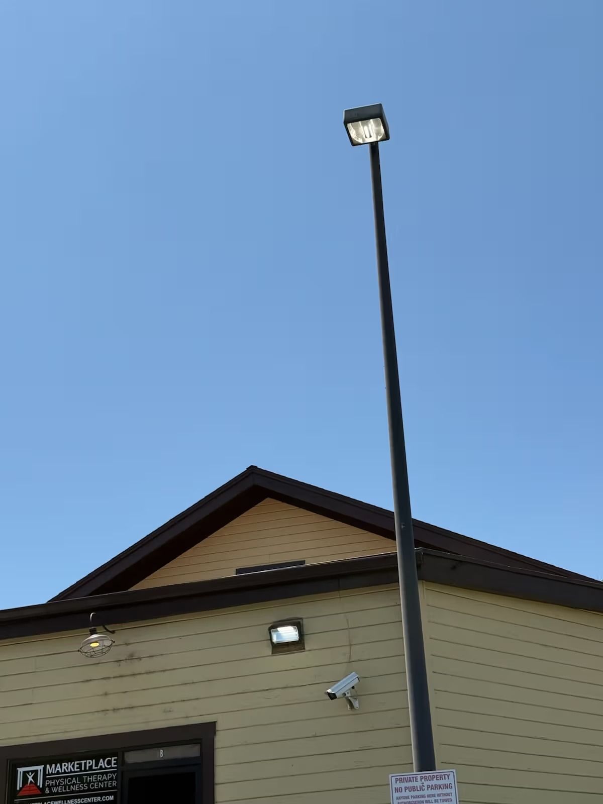 A tall black light pole with a square LED light against a clear blue sky and building.