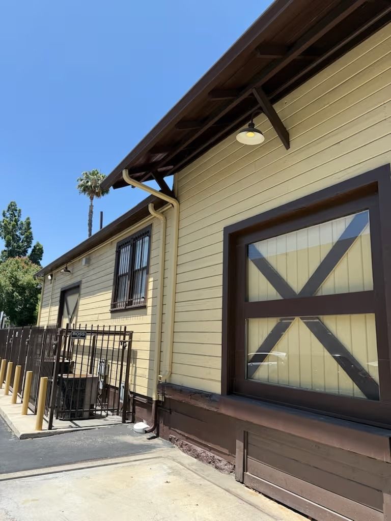 Tan building with brown trim and X-shaped window bars, outdoors on a sunny day.