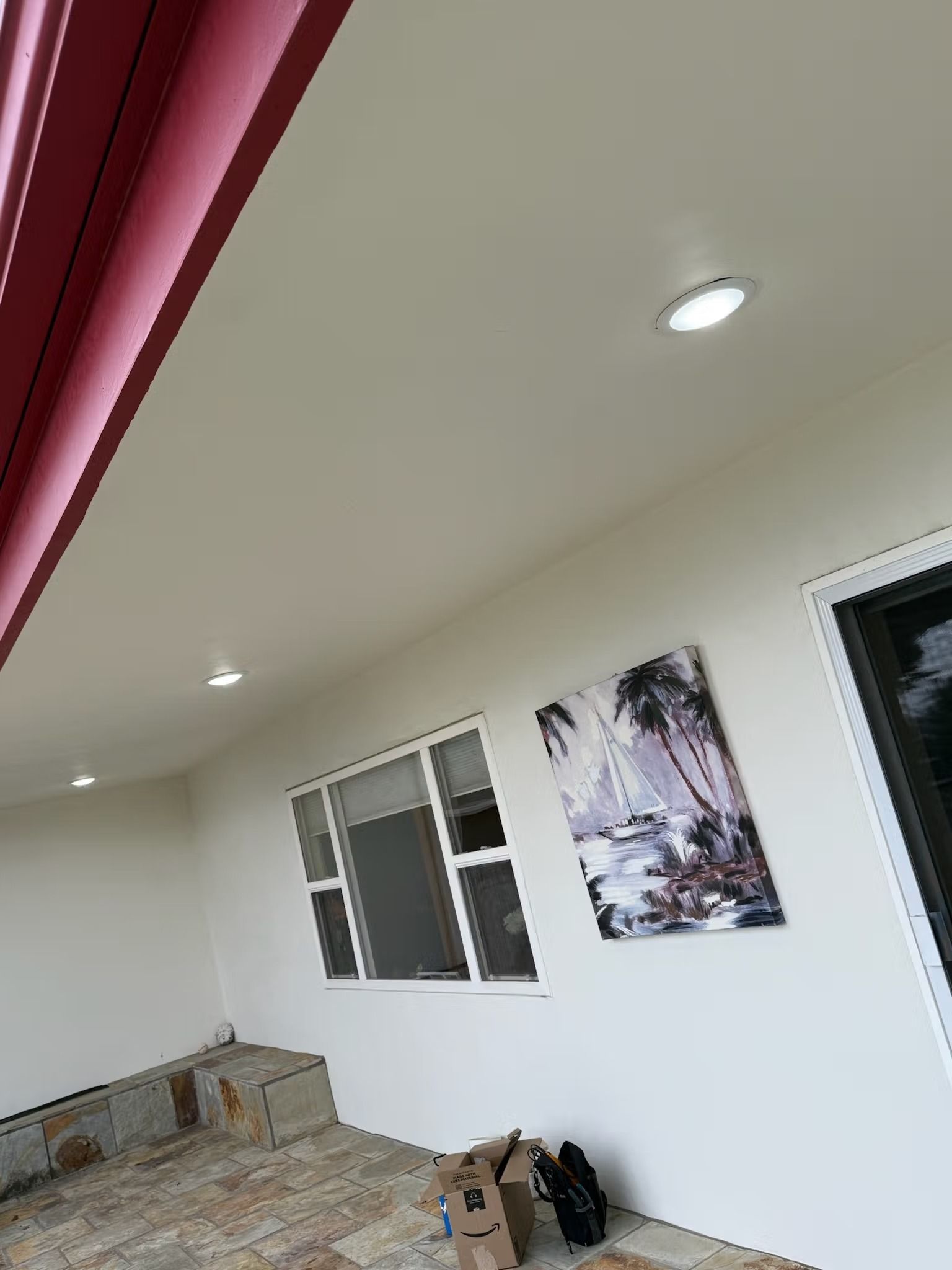 Exterior view of a porch with white walls, a window, and artwork. Recessed lights illuminate the ceiling.