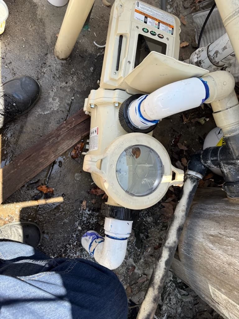 Pool pump with clear lid and plumbing connections, set against a concrete surface.