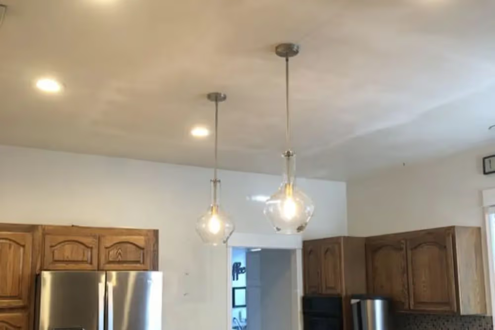 Two pendant lights hang over a kitchen with brown cabinets and stainless steel appliances.