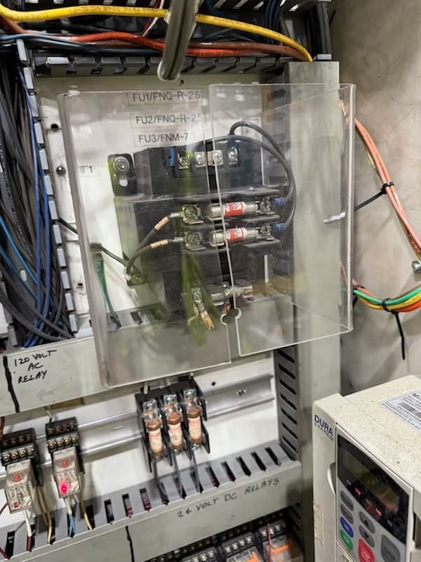 Electrical panel with fuses, relays, and wiring behind a clear protective cover.