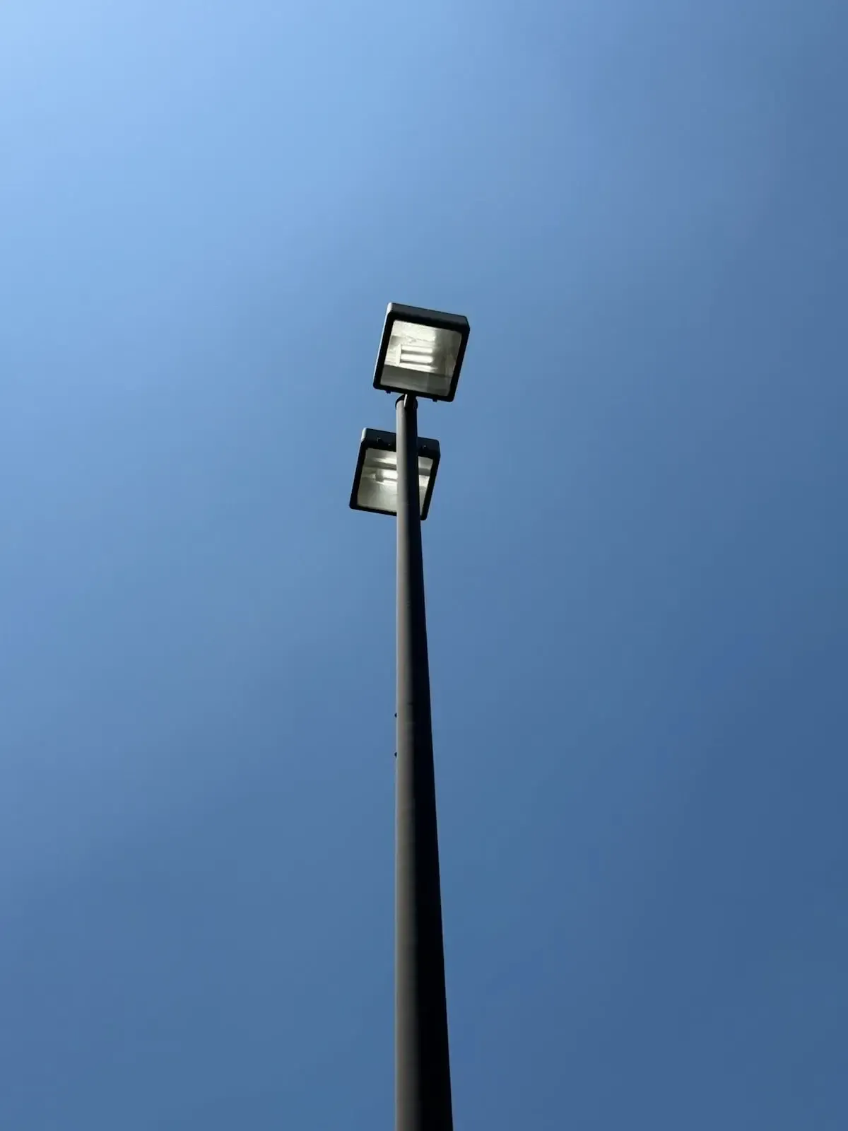 Tall light pole with two rectangular lights against a clear, blue sky.