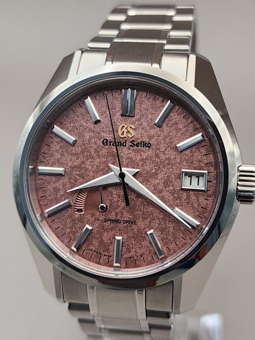 A silver watch with a pink face is sitting on a table.