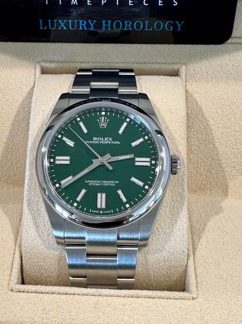 A silver watch with a green face is in a box that says luxury horology