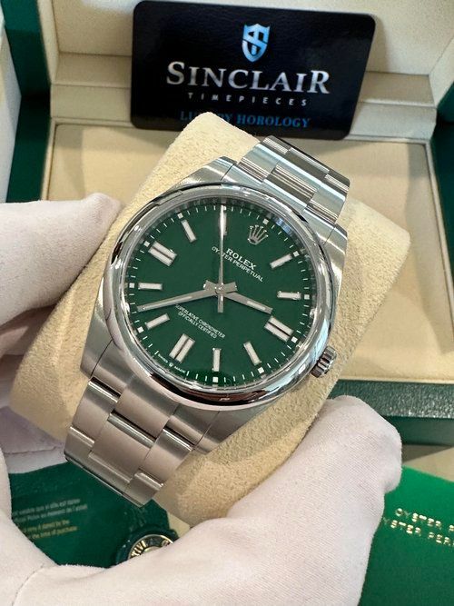 A person is holding a rolex watch with a green face