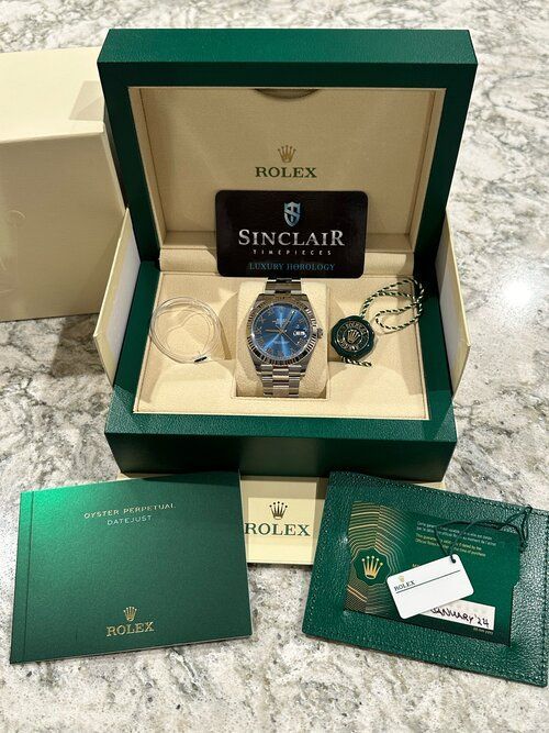 A rolex watch is in a green box on a counter.