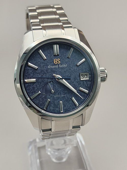 A silver watch with a blue face is sitting on top of a clear display case.