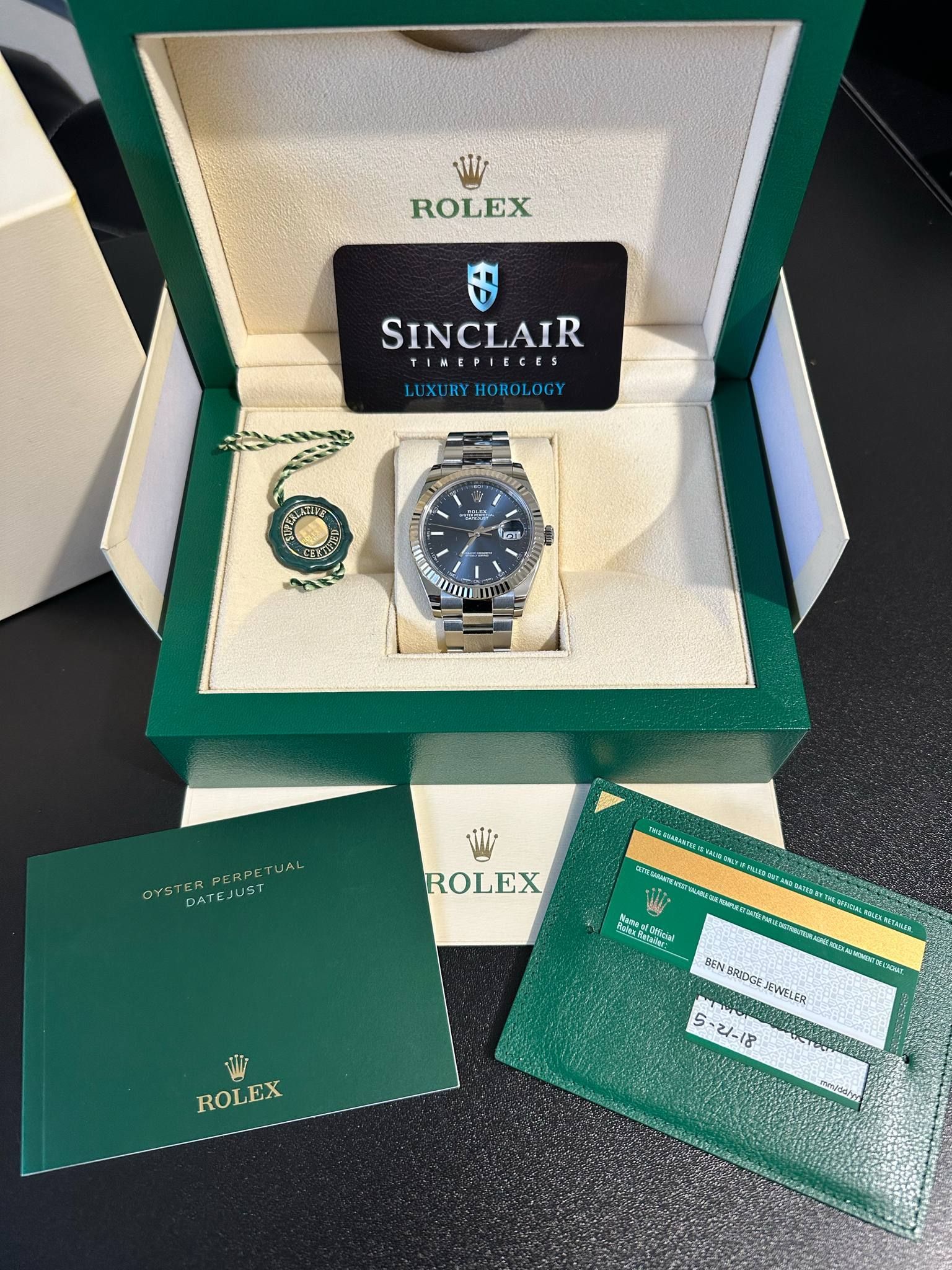 A rolex watch is in a green box with a sinclair card
