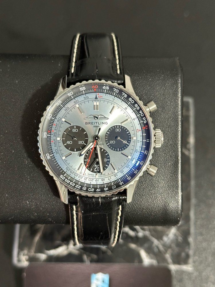 A silver watch with a black leather band is sitting on a black wrist.