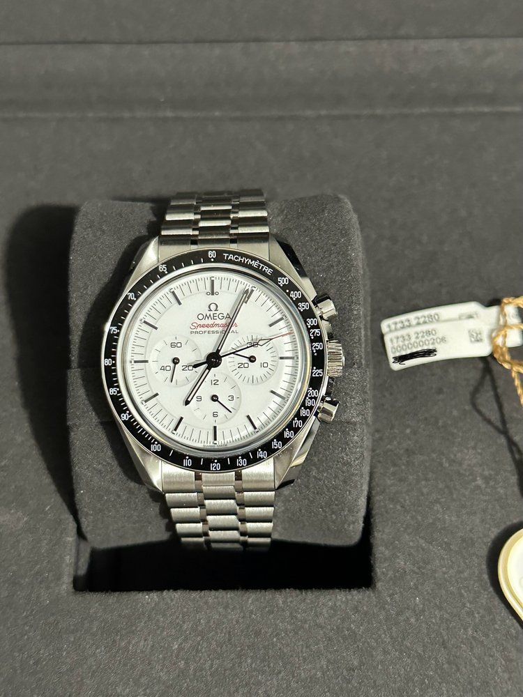 A silver watch with a white face is sitting on a black cushion.