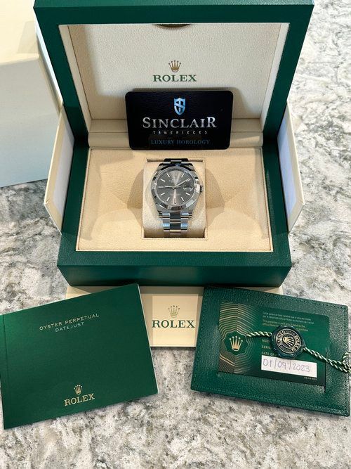 A rolex watch is in a green box on a table.