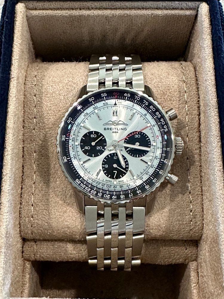 A silver watch is sitting on top of a brown cushion in a box.