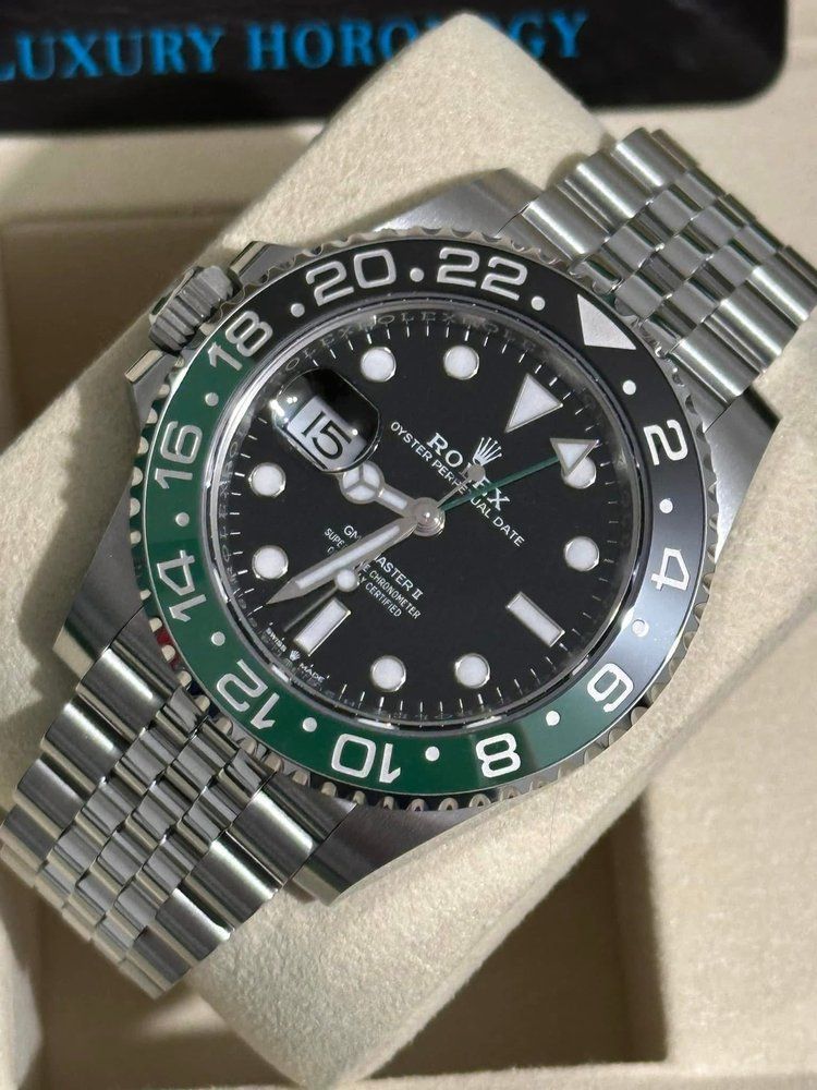 A silver and green rolex watch sits in a box