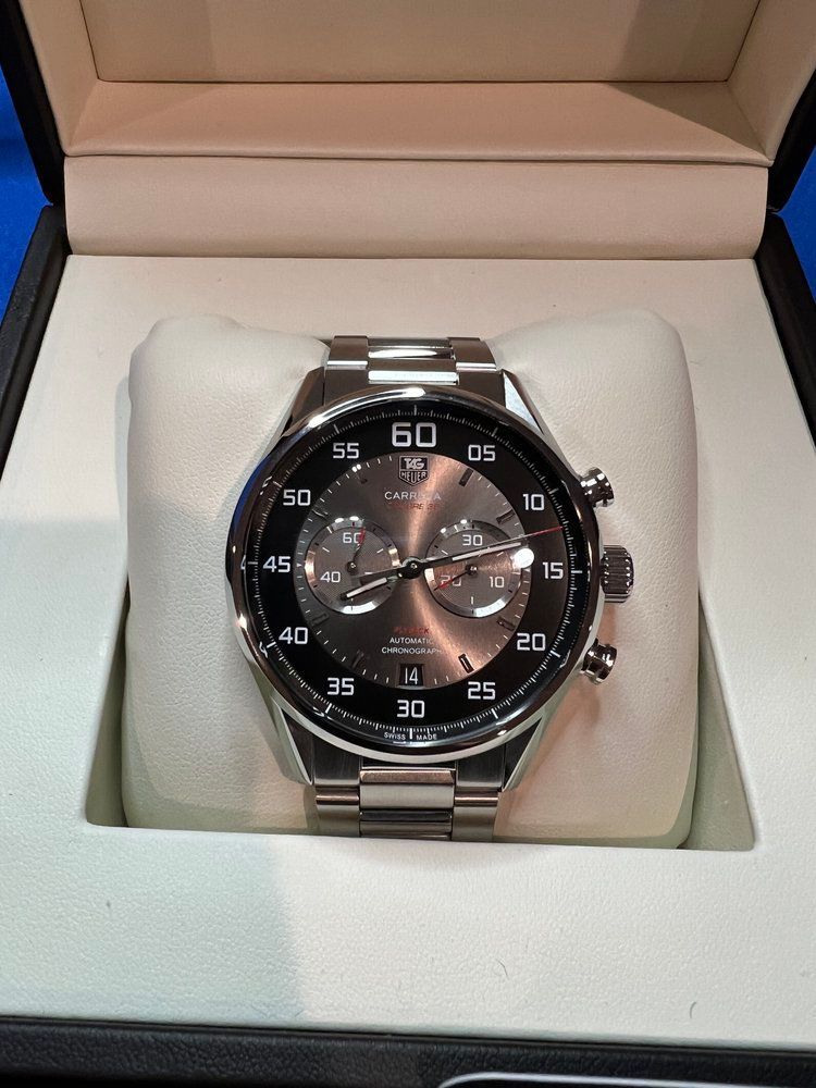 A silver watch is sitting on a white pillow in a box