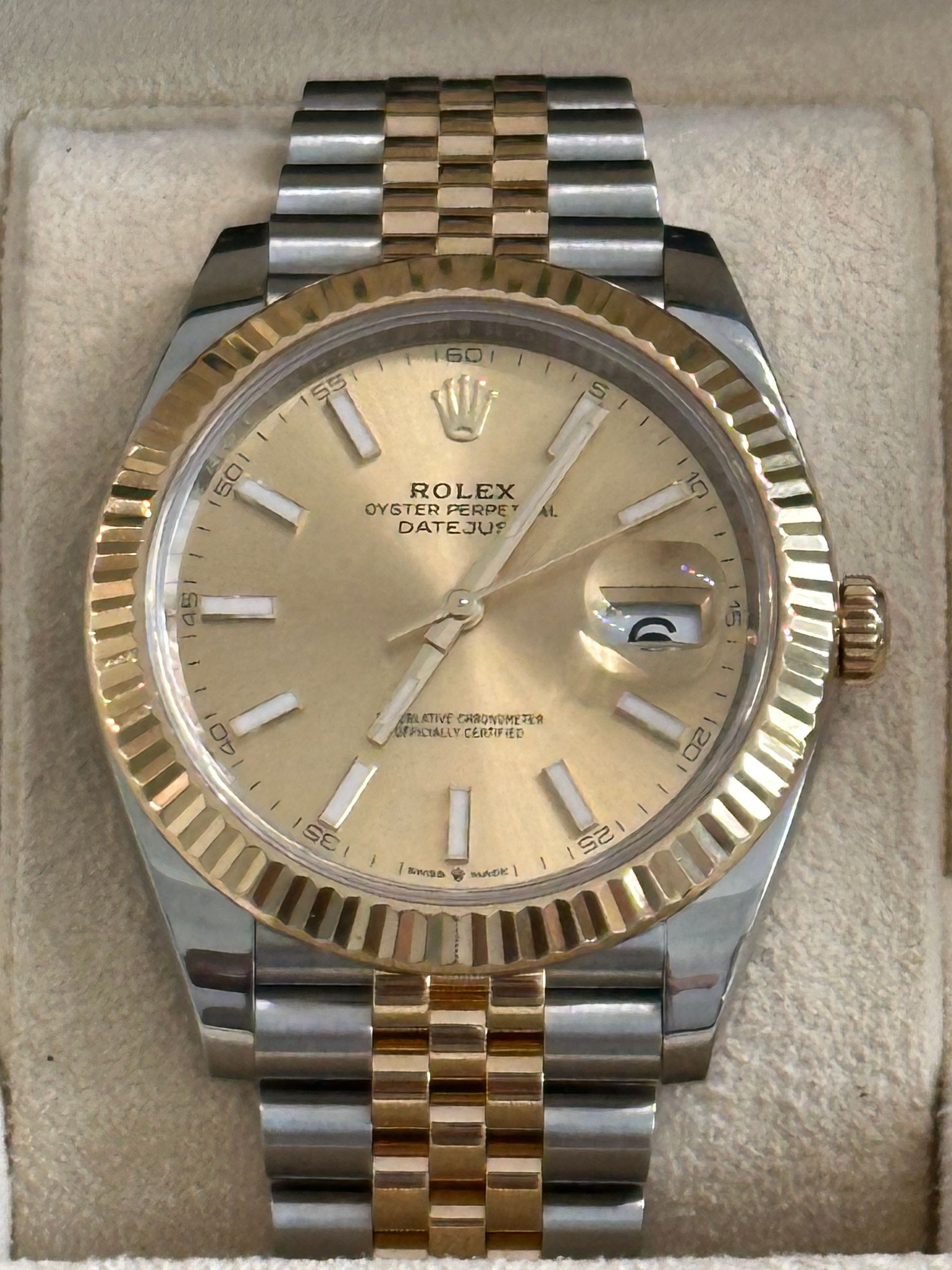 A rolex watch is in a green box on a table.