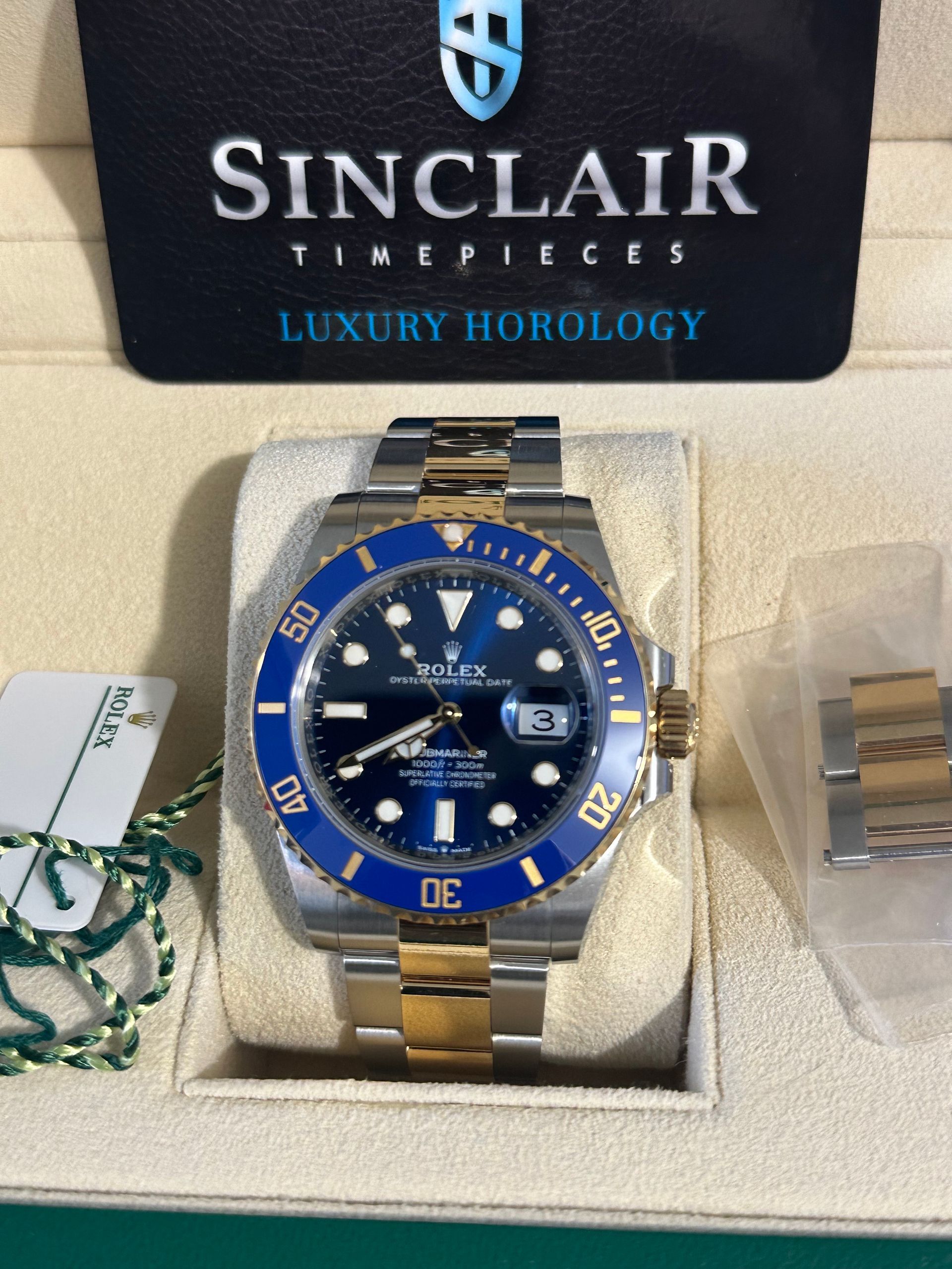 A rolex watch is in a green box with a sinclair card