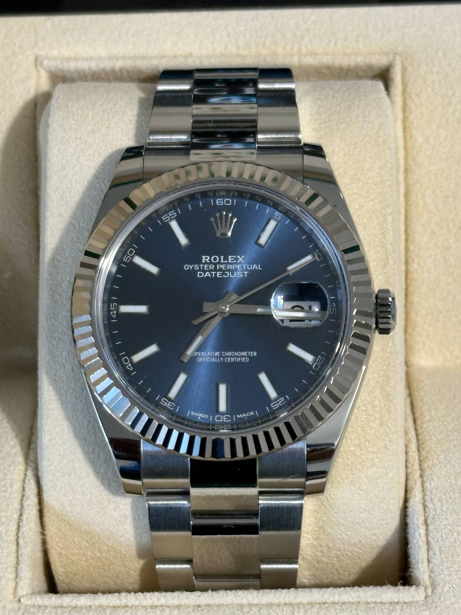 A silver and green rolex watch sits in a box