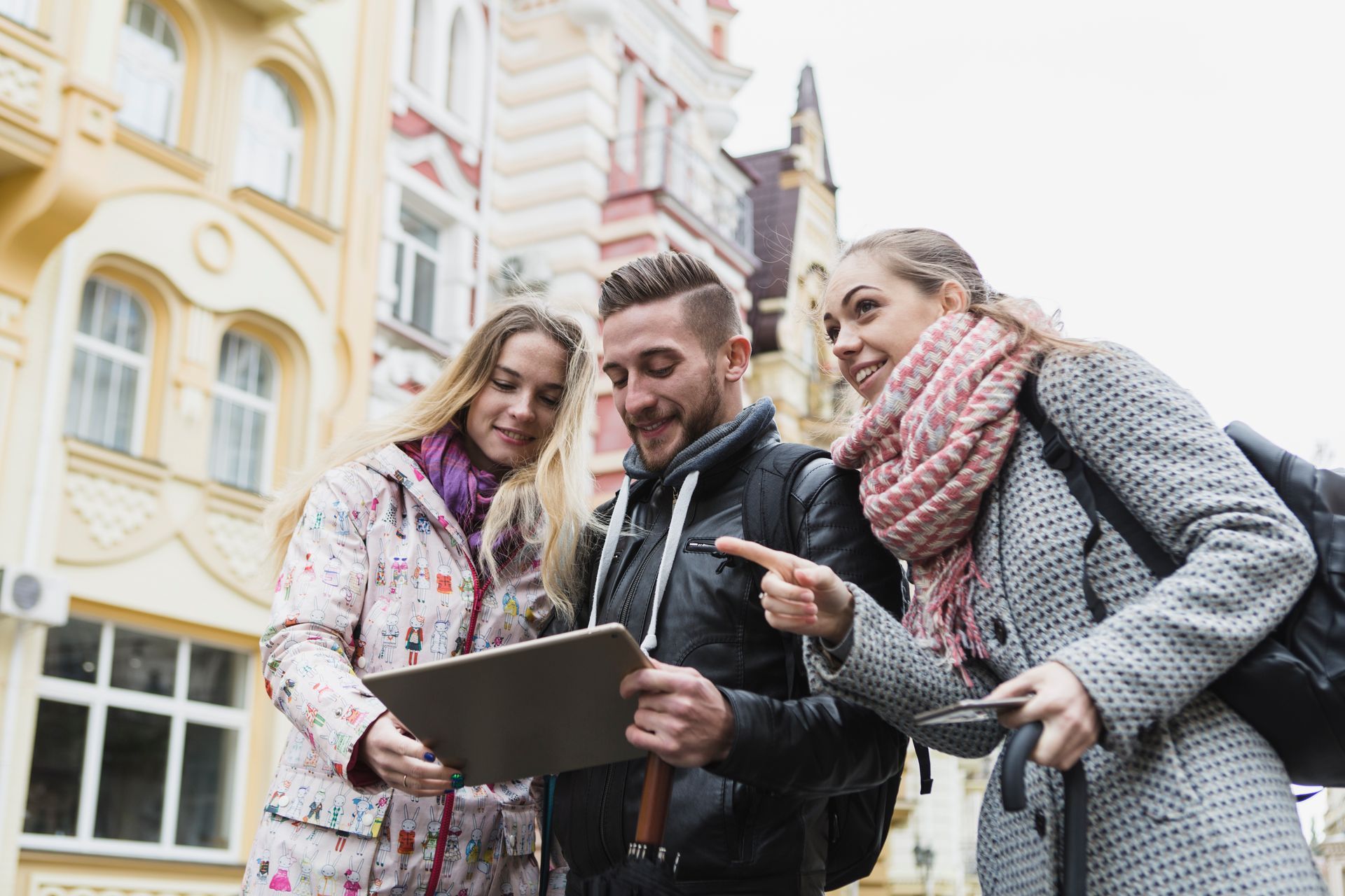 A man and two women are looking at a tablet in front of a building.