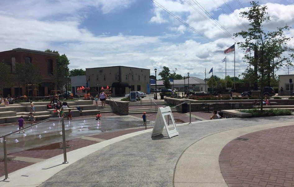 A group of people are playing in a fountain in a park.
