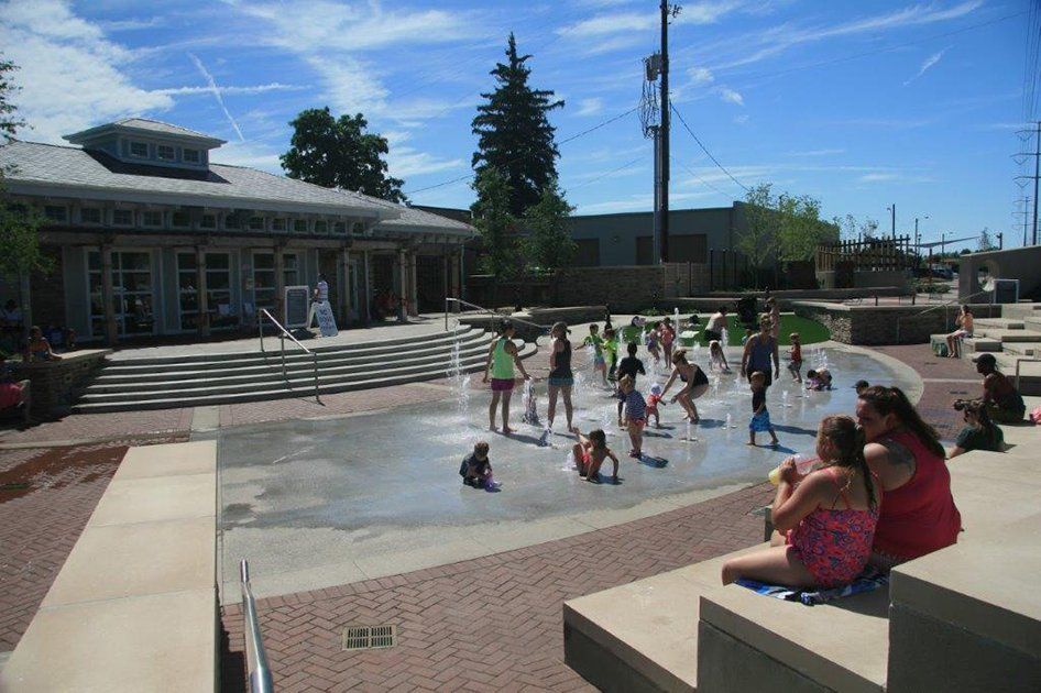 A group of children are playing in a fountain in front of a building.