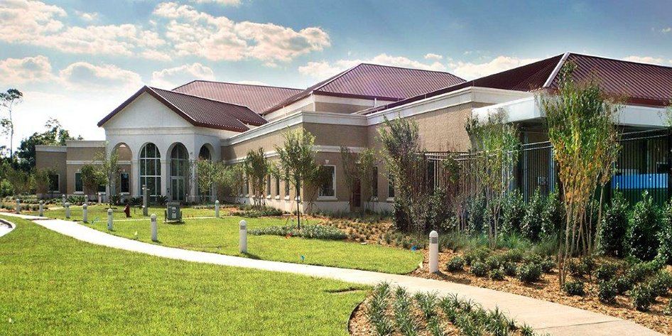 A large building with a red tile roof is surrounded by grass and trees.