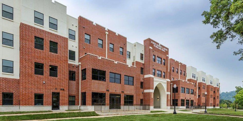 A large brick building with a lot of windows is sitting on top of a lush green field.
