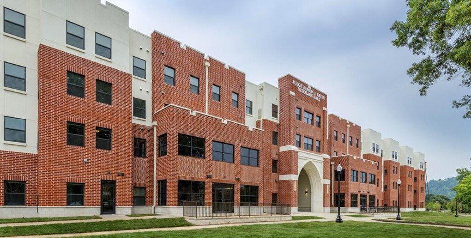 A large brick building with a lot of windows is sitting on top of a lush green field.