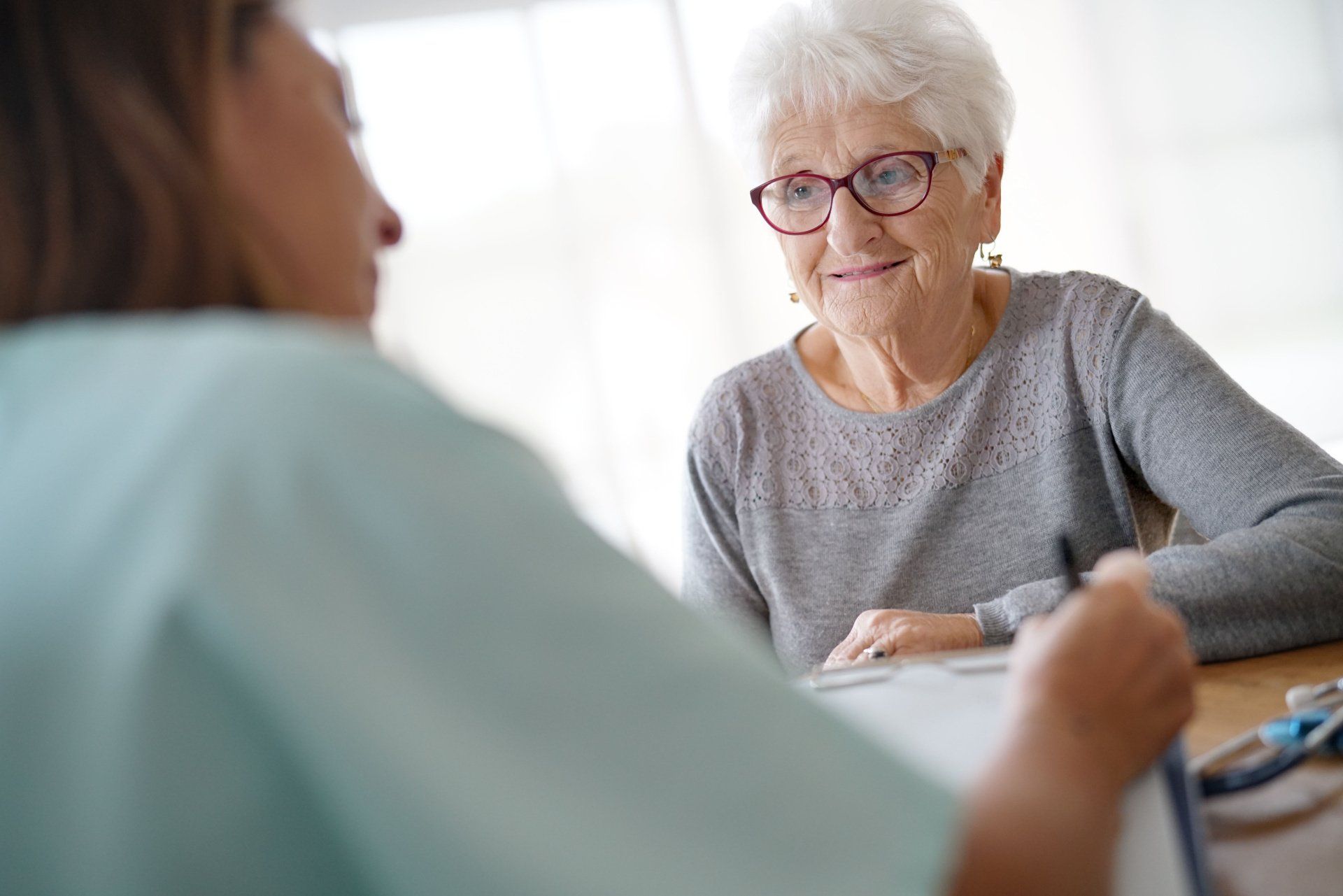 An elderly woman is sitting at a table talking to a nurse.