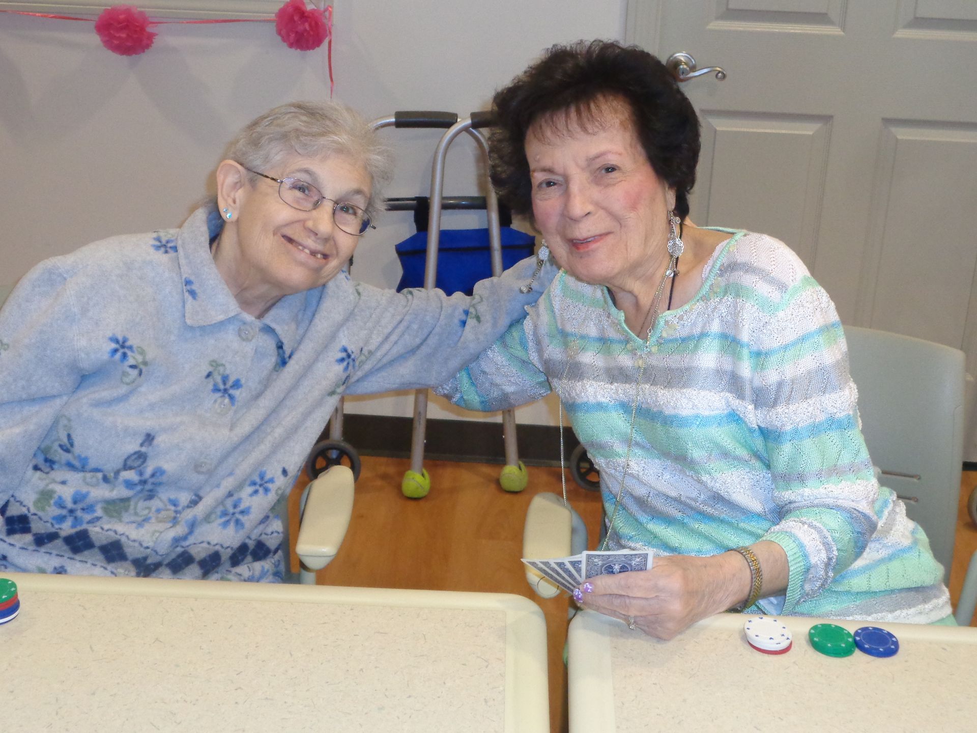 Two elderly women are posing for a picture while playing cards
