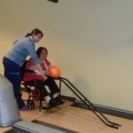 A woman in a wheelchair is playing bowling with another woman.
